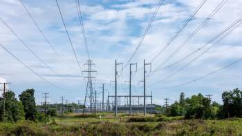 Power lines and transmission towers are visible in an open area with a cloudy sky in the background.