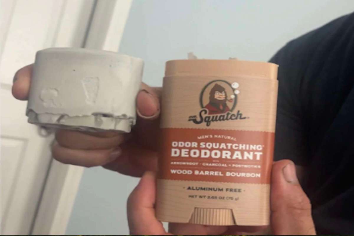 A person holds two deodorant containers, one gray and one brown labeled "Wood Barrel Bourbon."