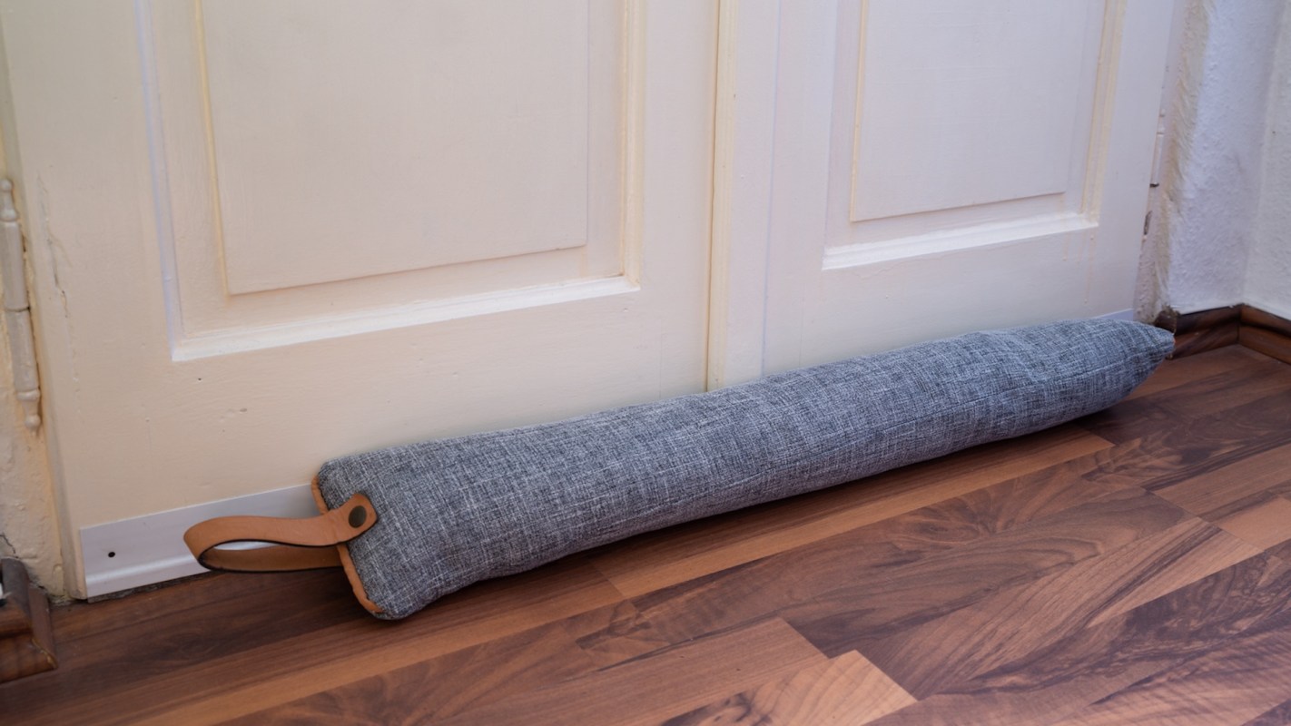 A fabric doorstop rests against a closed door on a wooden floor.