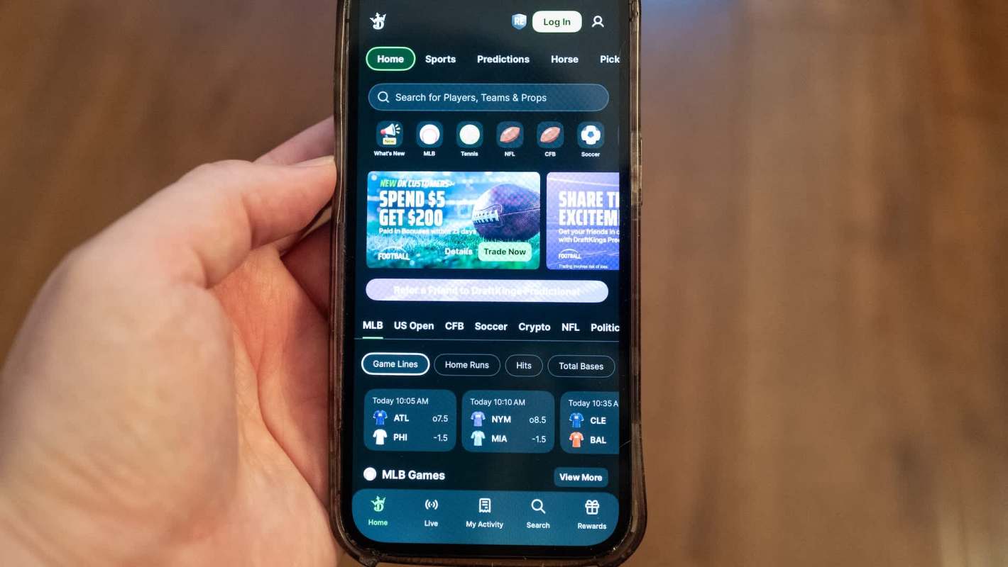 A hand holding a smartphone displaying the DraftKings sports betting app interface.
