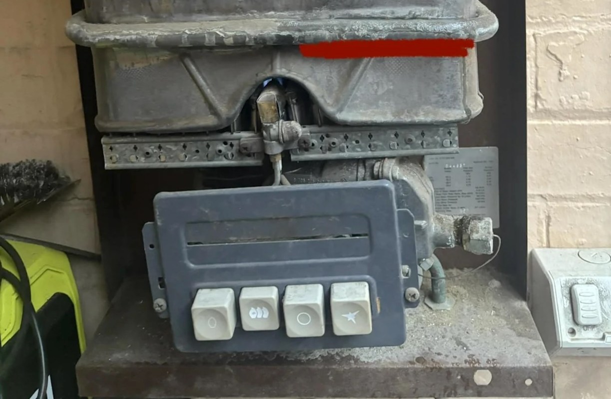 A gas appliance control panel with buttons and connected pipes, surrounded by dust.