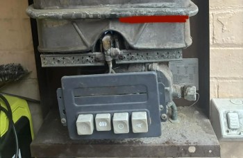 A gas appliance control panel with buttons and connected pipes, surrounded by dust.