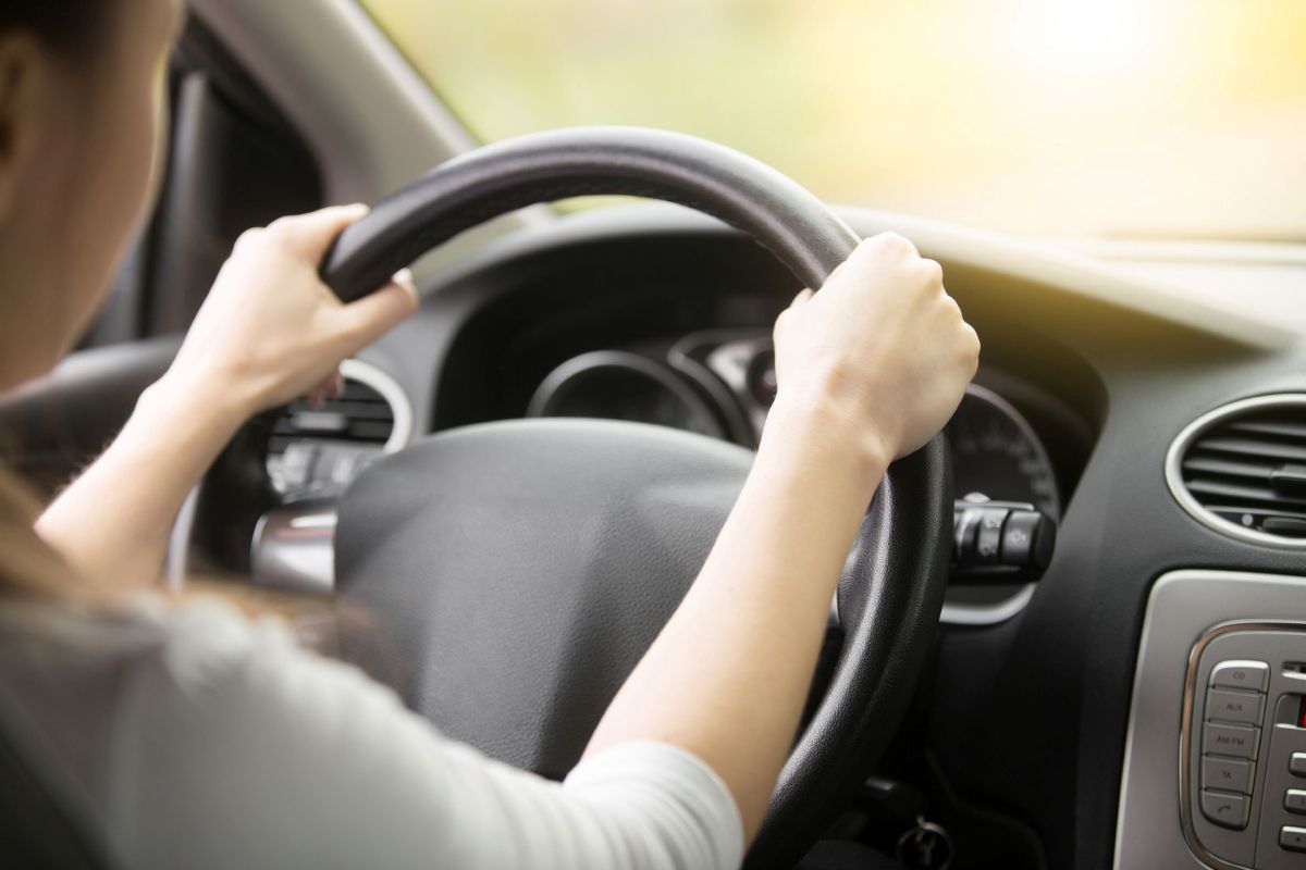 A female driver has her hands at 10 and 2 on a steering wheel inside a vehicle