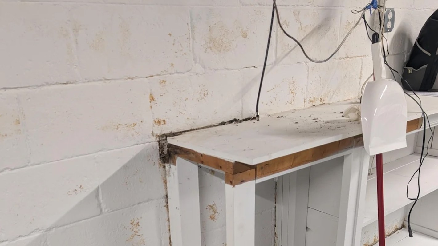 A white wall with stains alongside a wooden table, a dustpan, and wires hanging above.
