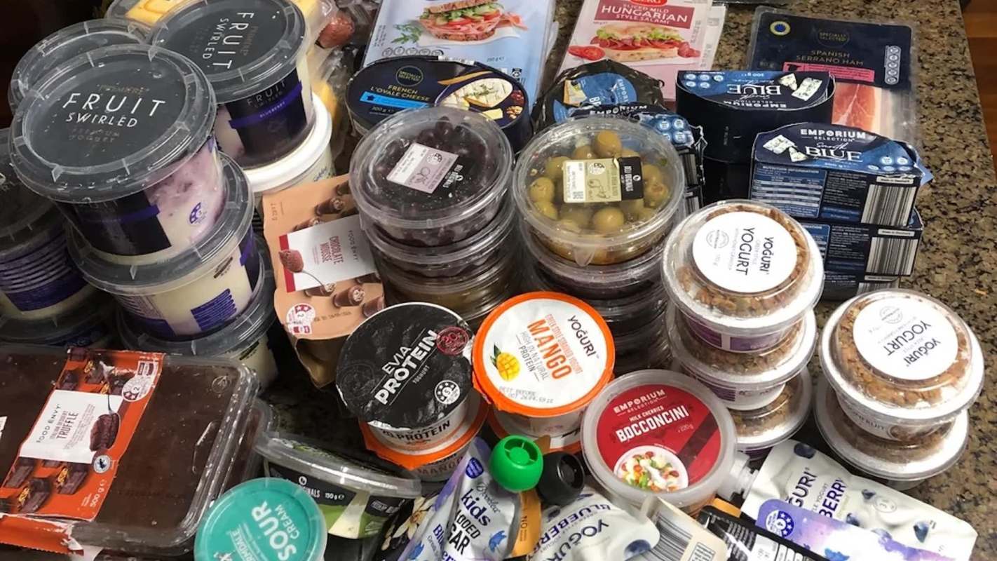 An assortment of various food items, including yogurt, granola, and packaged meats, on a countertop.