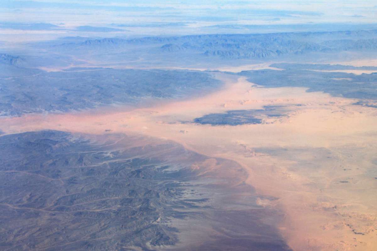 Aerial view of a vast desert landscape with mountains in the background and a pale sandy area.