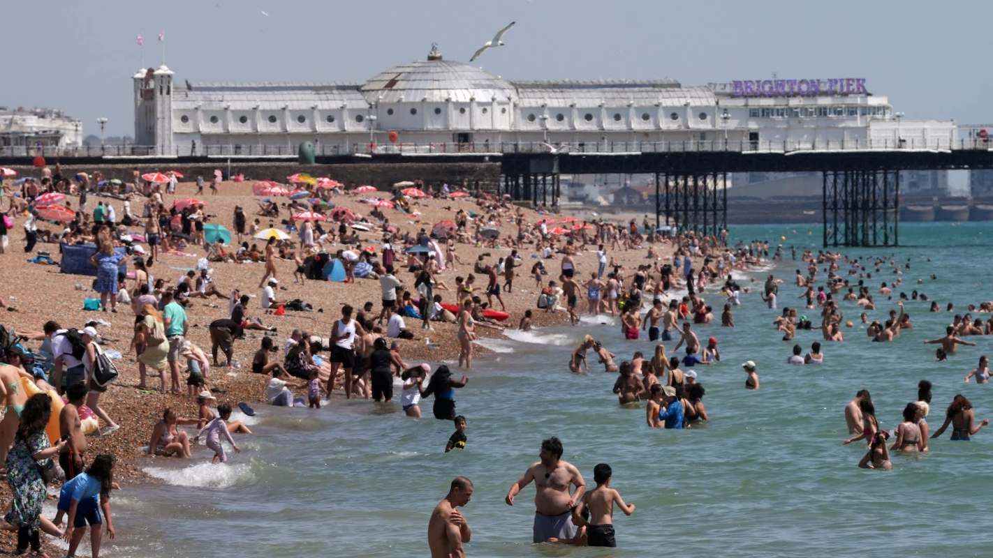 A busy beach scene with numerous people swimming and sunbathing near Brighton Pier.