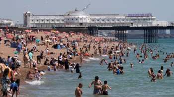 A busy beach scene with numerous people swimming and sunbathing near Brighton Pier.
