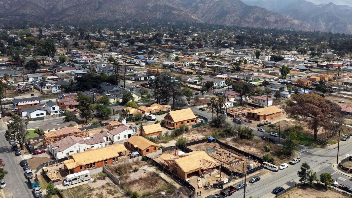 Aerial view of a suburban area featuring houses, construction sites, and mountain ranges in the background.