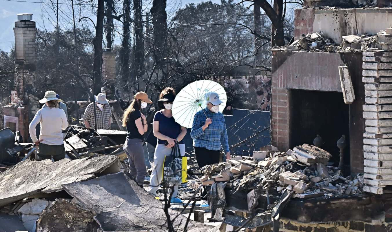 Several people explore a site with debris and remnants of structures, surrounded by burned trees.
