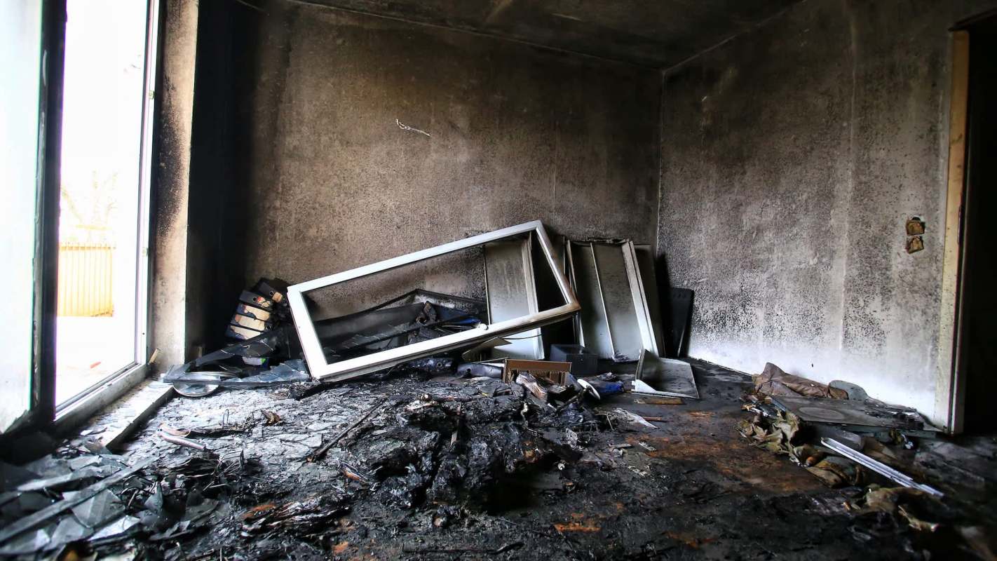 A room with charred debris, burned furniture, and soot-covered walls.