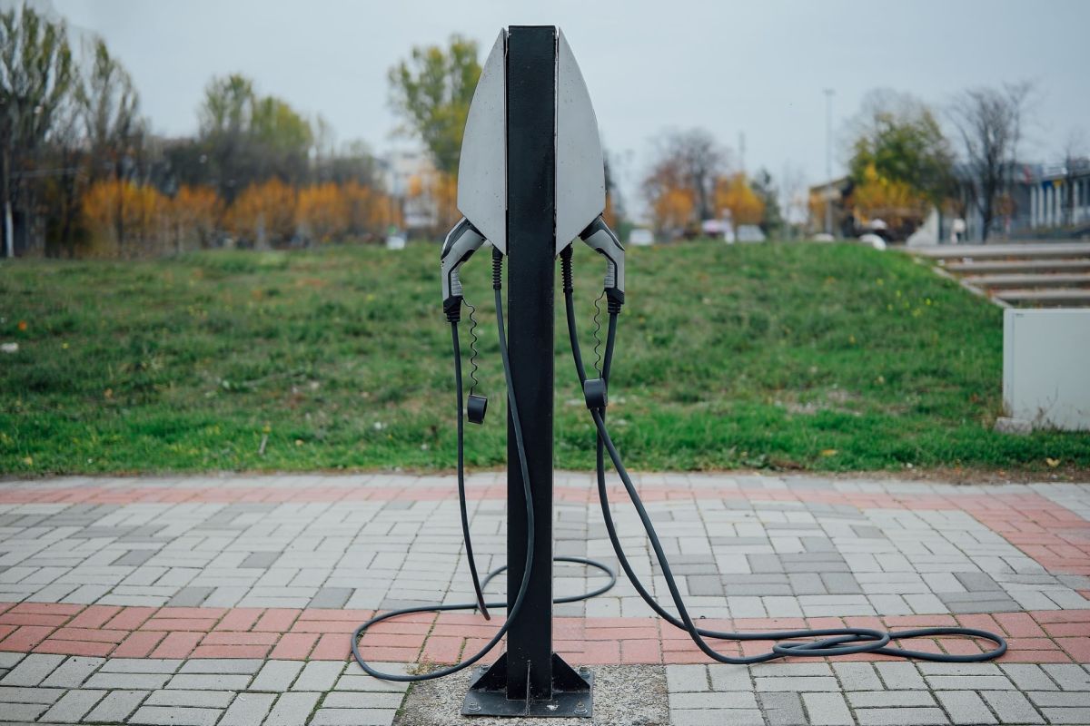 An electric vehicle charging station with two connectors on a paved surface and green grass in the background.