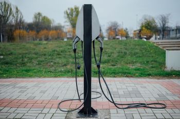 An electric vehicle charging station with two connectors on a paved surface and green grass in the background.