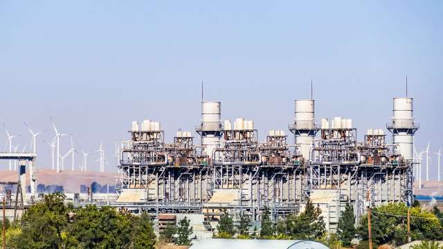 A power plant with multiple turbine structures and wind turbines in the background.