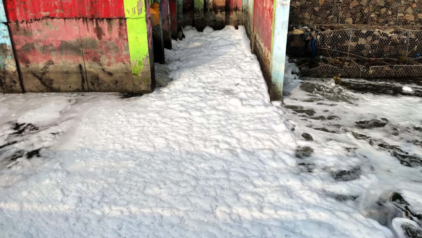 A waterway covered in white foam near colorful concrete walls.