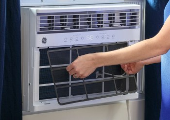 A person removing a filter from an air conditioning unit.