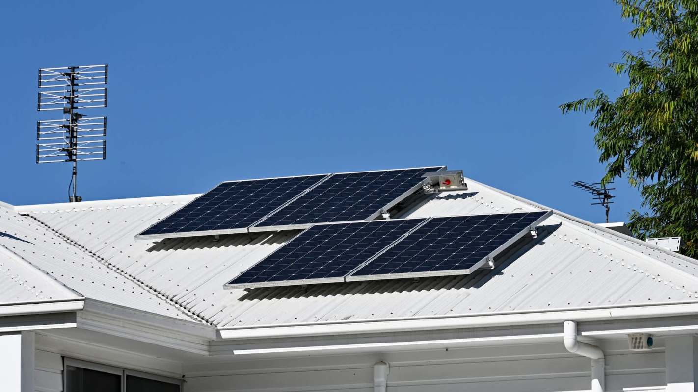 Solar panels installed on a white roof under a clear blue sky.