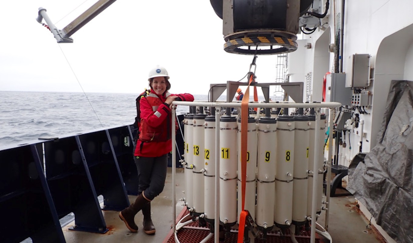 A person stands next to a large scientific instrument on a research vessel in the ocean.