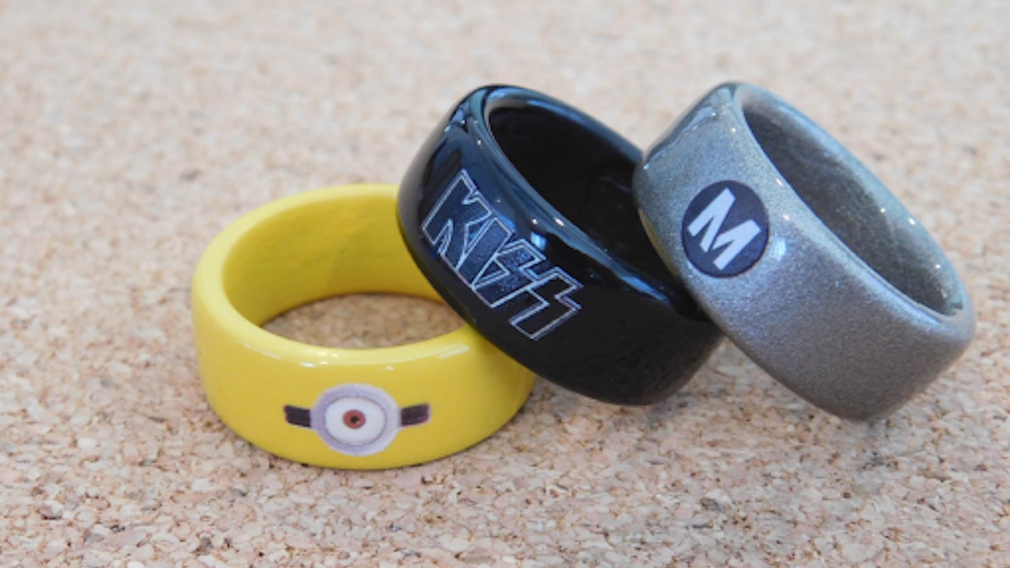 Three rings in yellow, black, and silver on a cork background, featuring graphics and logos.