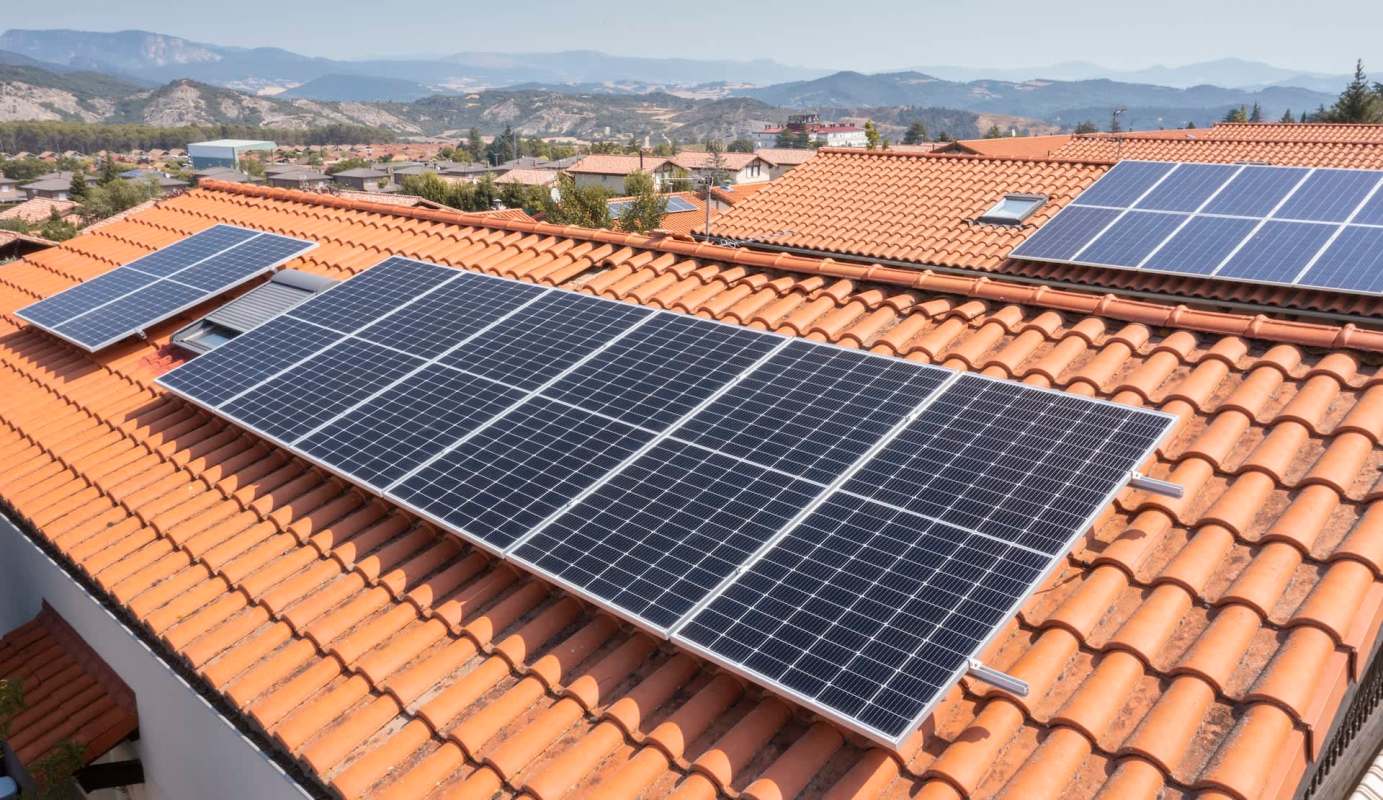 Solar panels installed on a terracotta tiled roof with mountains in the background.