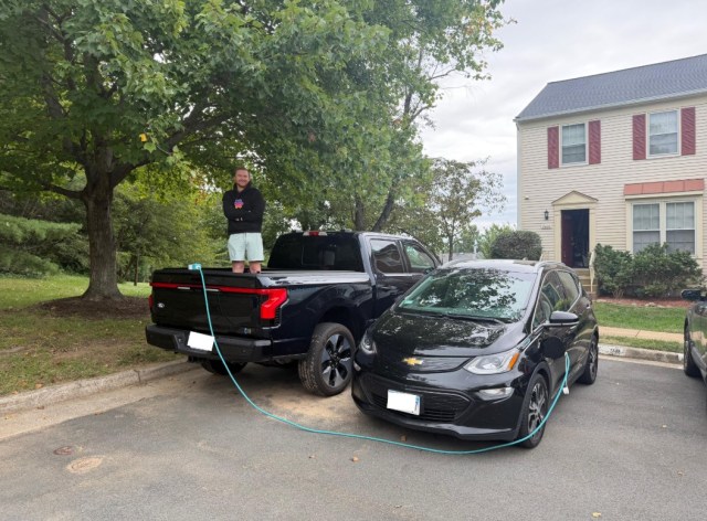 An F-150 next to a Bolt with a charging cable connecting them.