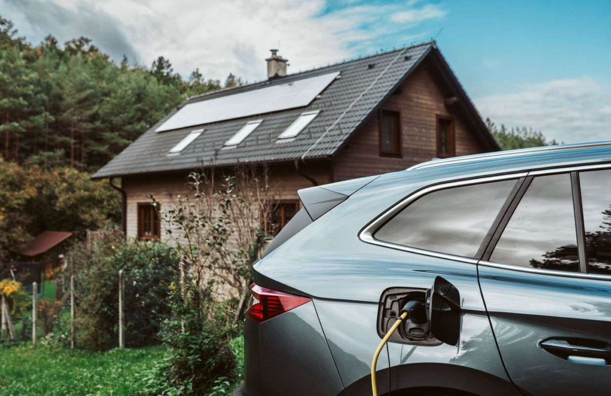 An EV charging near a home with solar panels.
