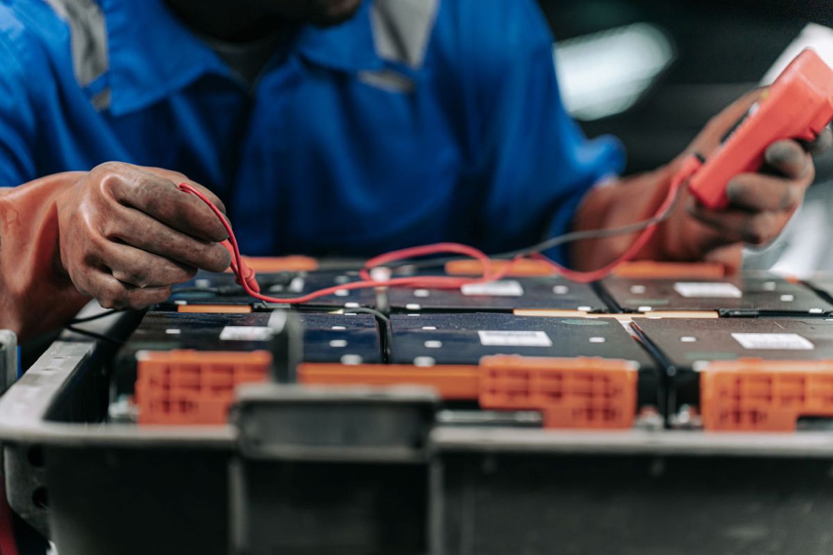A person tests batteries using a multimeter in a workshop.