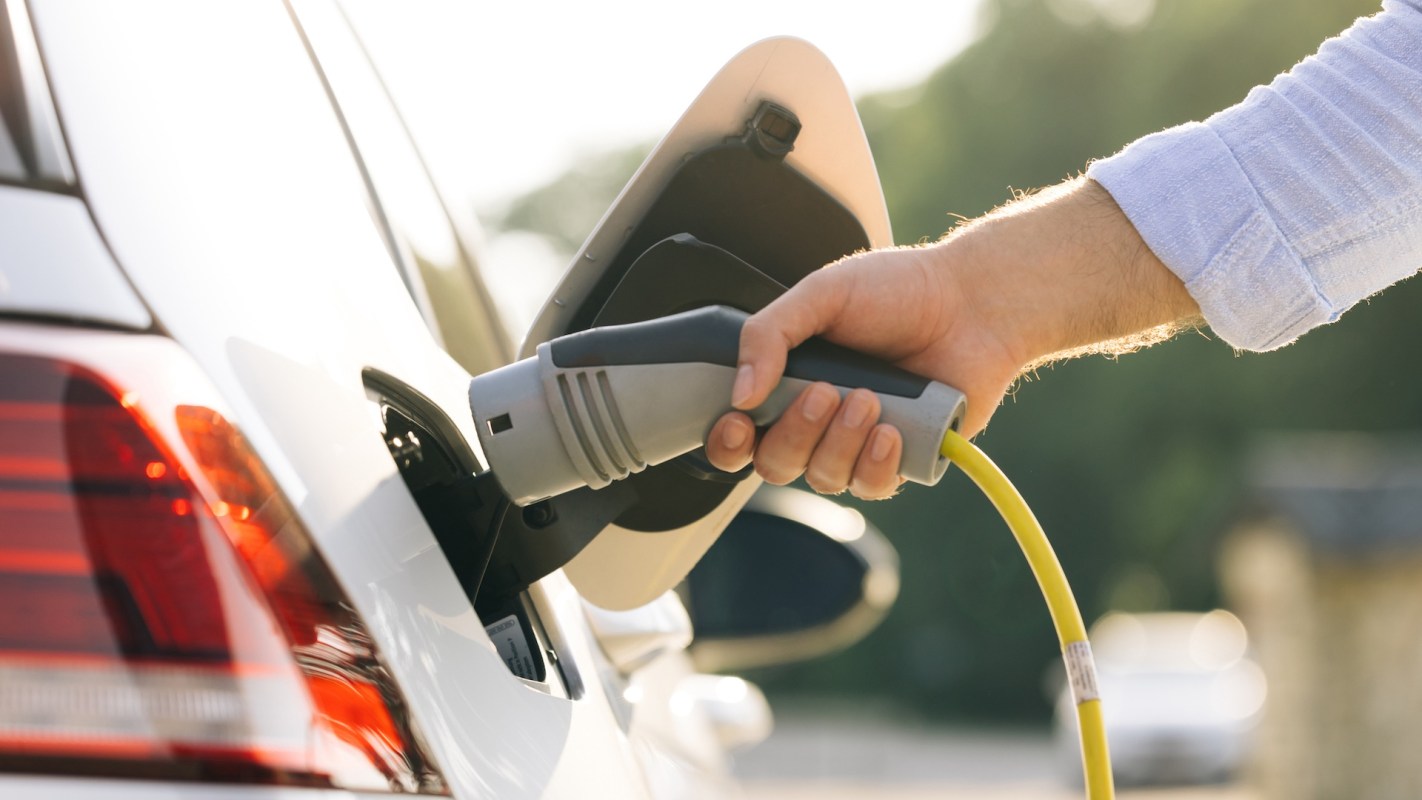 A hand connects an electric charging cable to a car for charging.