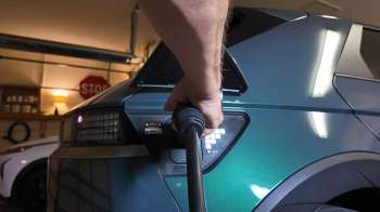 A person connects a charging cable to the rear of an electric vehicle in a garage.