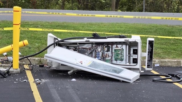 An overturned EV charging station with its contents spilled out and caution tape surrounding the area.