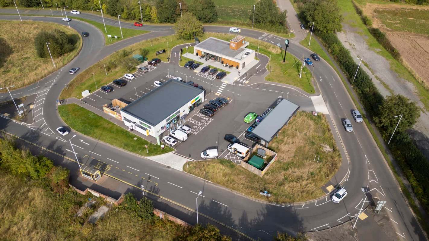 An aerial view of a circular road with a retail complex and parked vehicles.