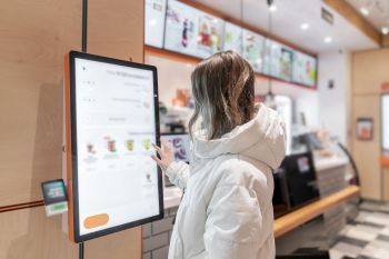 A woman stands at a screen in a fast food restaurant to select food from a menu