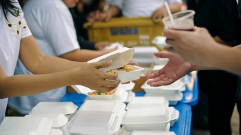 A person hands a food container to another person at an outdoor event with multiple containers visible.