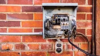 An electrical panel mounted on a brick wall with exposed wiring and outlets.