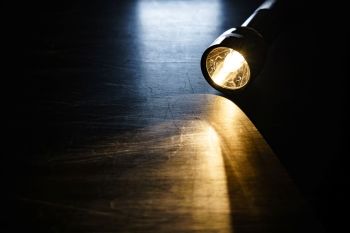 A lit flashlight on a wooden table.