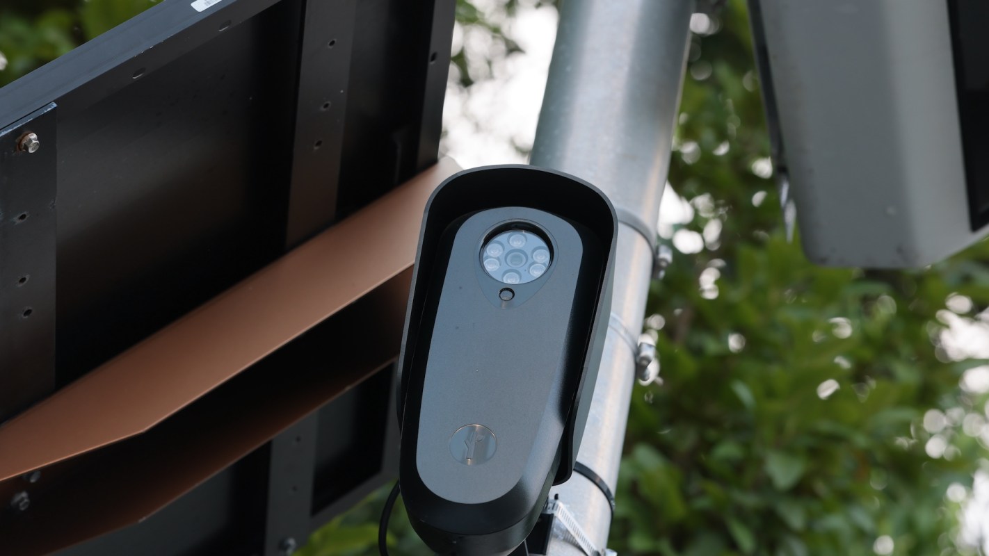 A traffic camera mounted on a pole with surrounding greenery.