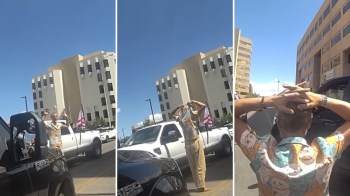 A man stands between two vehicles on a city street, raising his hands with a building in the background.
