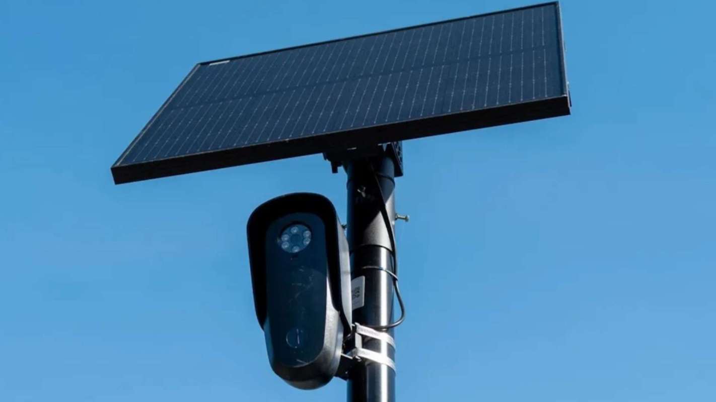 A solar panel mounted on a pole next to a black camera.