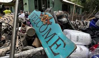 A weathered "Welcome" sign surrounded by debris and discarded items after flood damage.
