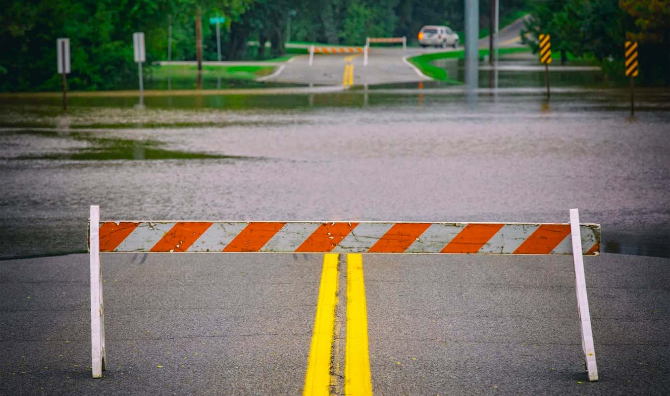 A road is flooded with water, obstructed by a barricade.