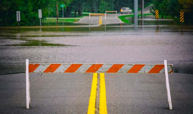 A road is flooded with water, obstructed by a barricade.