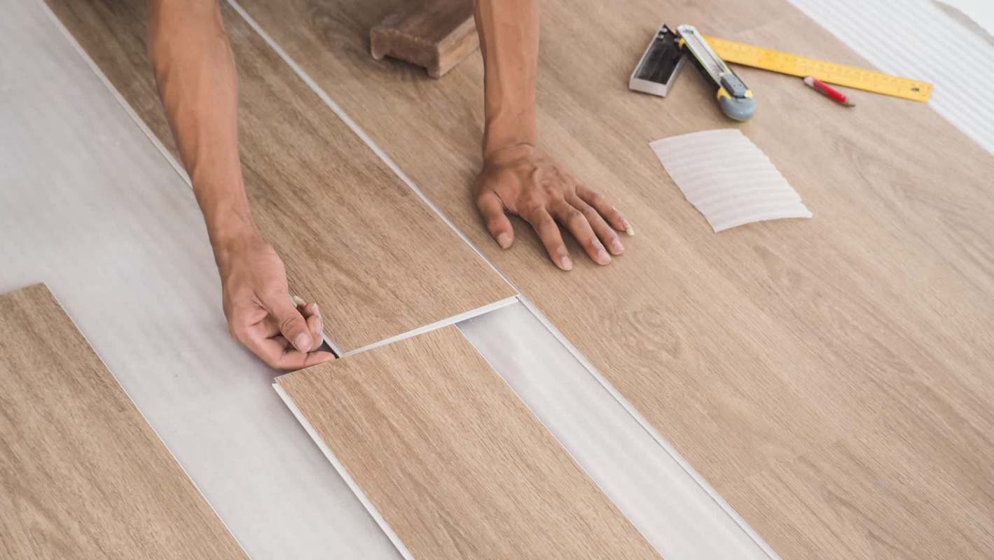 A person lays laminate vinyl flooring planks on a surface with measuring tools nearby.