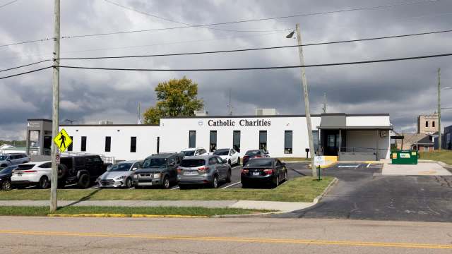 A building labeled "Catholic Charities" with parked cars and a pedestrian crossing sign nearby.