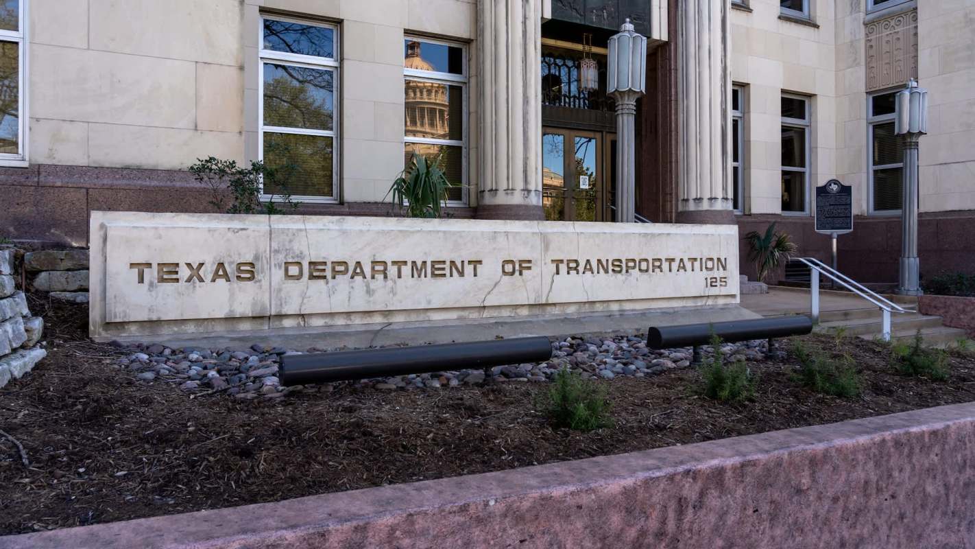 A stone sign for the Texas Department of Transportation in front of a building with decorative columns.