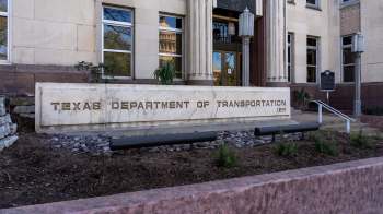 A stone sign for the Texas Department of Transportation in front of a building with decorative columns.