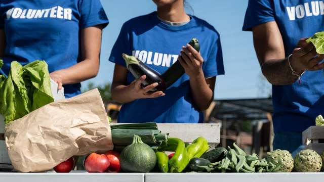 Volunteers holding vegetables and fruits at an outdoor table.
