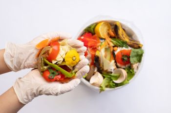 Gloved hands hold food scraps over a garbage bin of food scraps