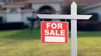 A "For Sale" sign in front of a house with a grassy lawn.