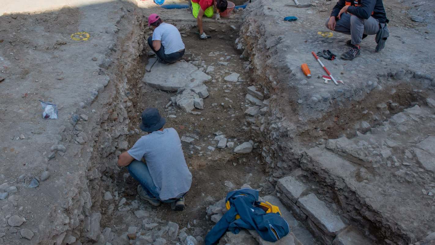 Several people are working in a rocky excavation site, uncovering layers of soil and stones.