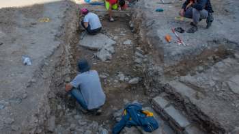 Several people are working in a rocky excavation site, uncovering layers of soil and stones.